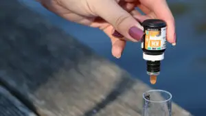Een hand druppelt KH-reagens in een buisje met vijverwater, om de carbonaathardheid te meten